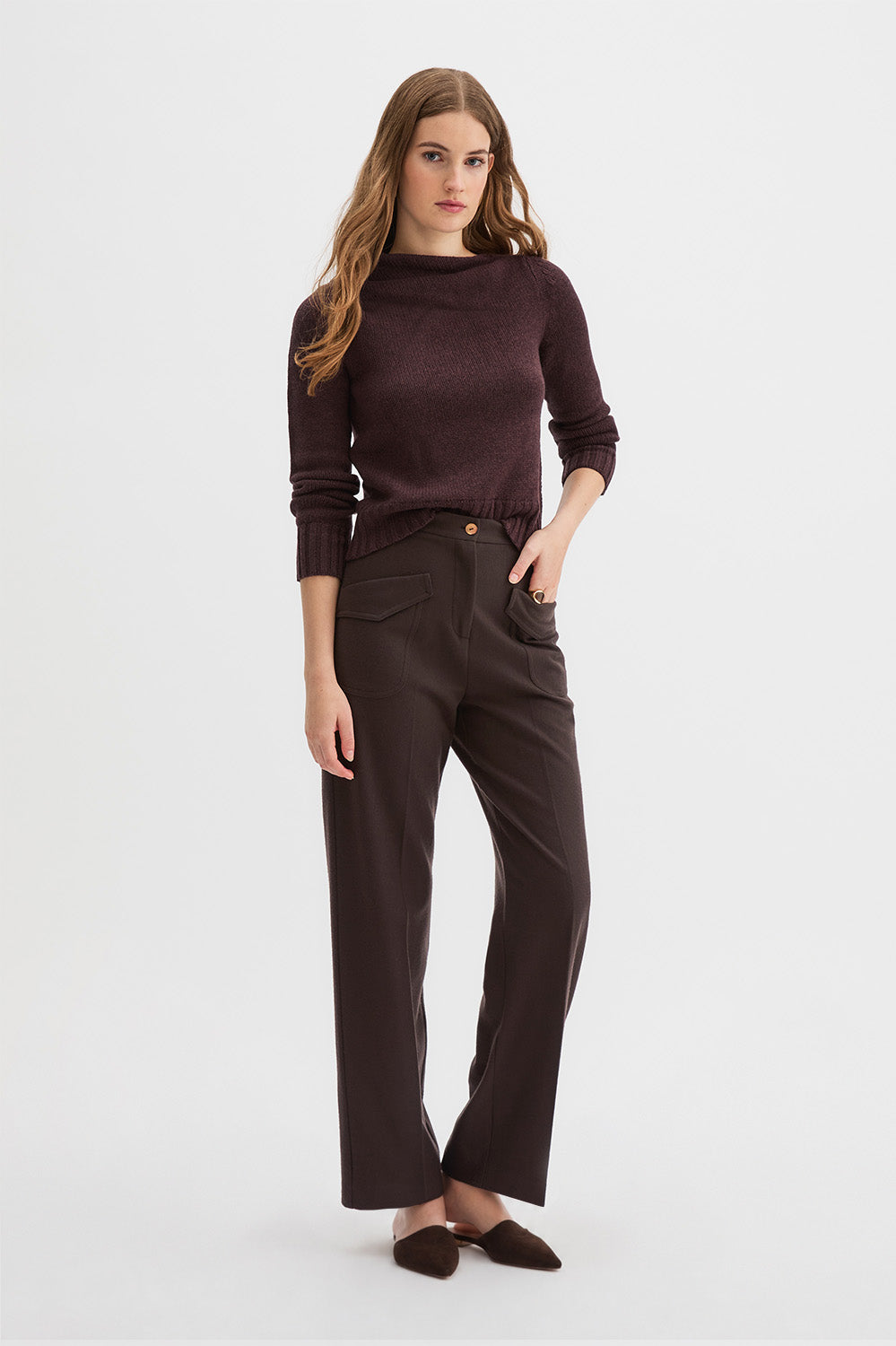 Hutton Trousers and Claude Knit. A woman modeling a dark plum long-sleeve knit top and dark brown wide-leg trousers against a light gray studio background.