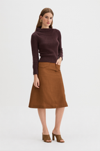 Claude Knit and Kingma A-Line Skirt. A woman modeling a dark plum ribbed knit mock-neck sweater and a brown A-line skirt, paired with brown heeled sandals, against a plain light gray studio background.