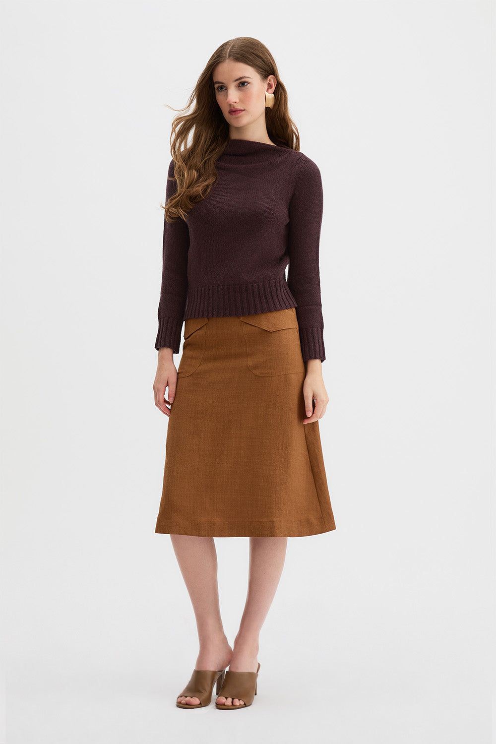 Claude Knit and Kingma A-Line Skirt. A woman modeling a dark brown draped knit sweater and a rust linen A-line skirt against a plain white studio background.