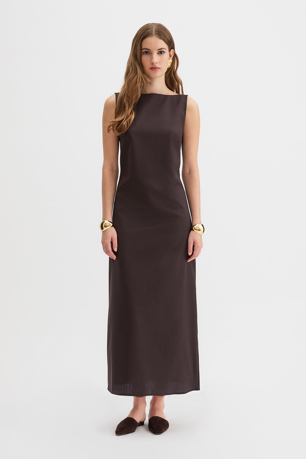 Yves Dress. A woman modeling a sleeveless, dark brown midi dress with a boat neckline, standing against a plain light gray studio background.