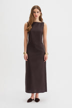Yves Dress. A woman modeling a sleeveless, dark brown midi dress with a boat neckline, standing against a plain light gray studio background.