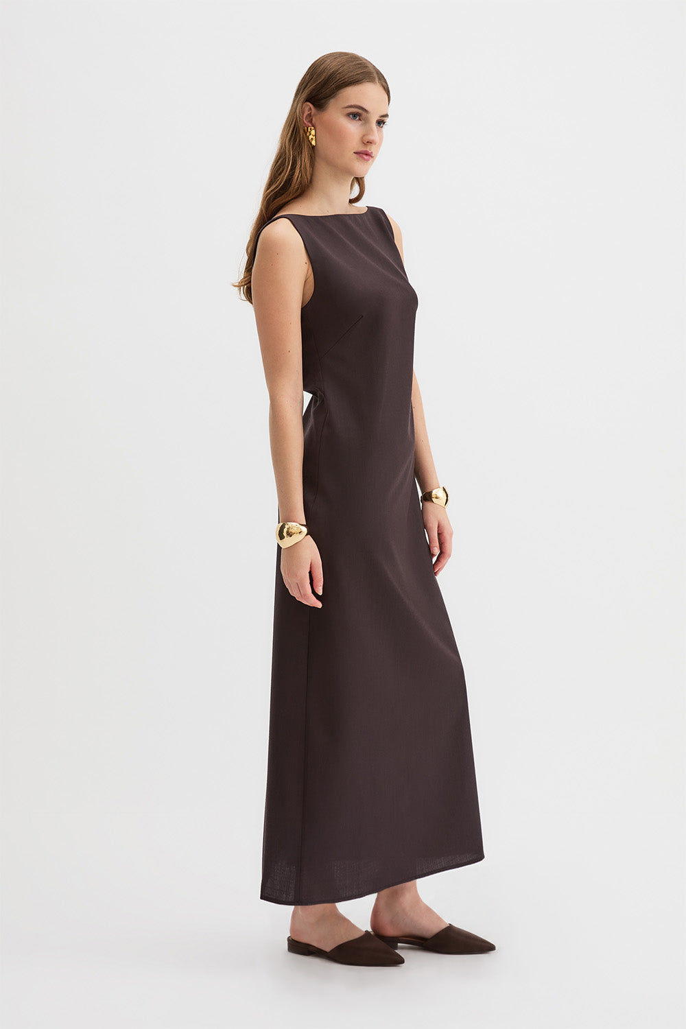 Yves Dress. A woman modeling a sleeveless, dark brown maxi dress with a boat neckline, photographed against a clean white studio background.